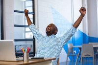 Attractive man with arms raised in success in front of laptop