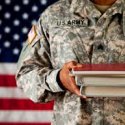 Military member holding textbooks in front of American flag