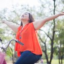 Pretty young girl on bicycle with arms oustretched with joy