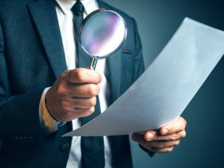 Man holding magnifying glass looking at paper